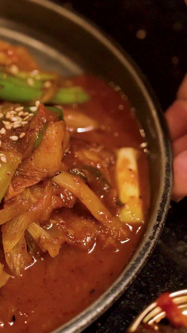 Foto close-up babi tumis pedas dengan kimchi dan daun bawang di restoran