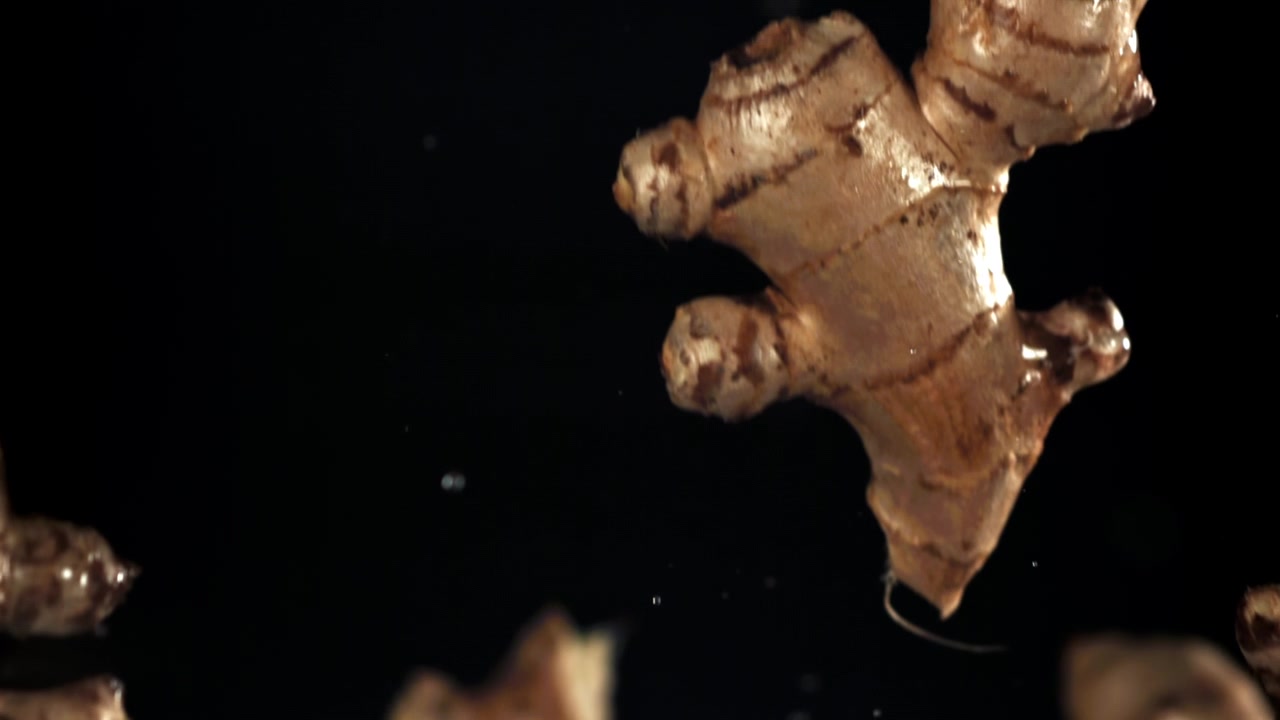 Ginger Roots Falling with Water Droplets on Black Background in Slow Motion