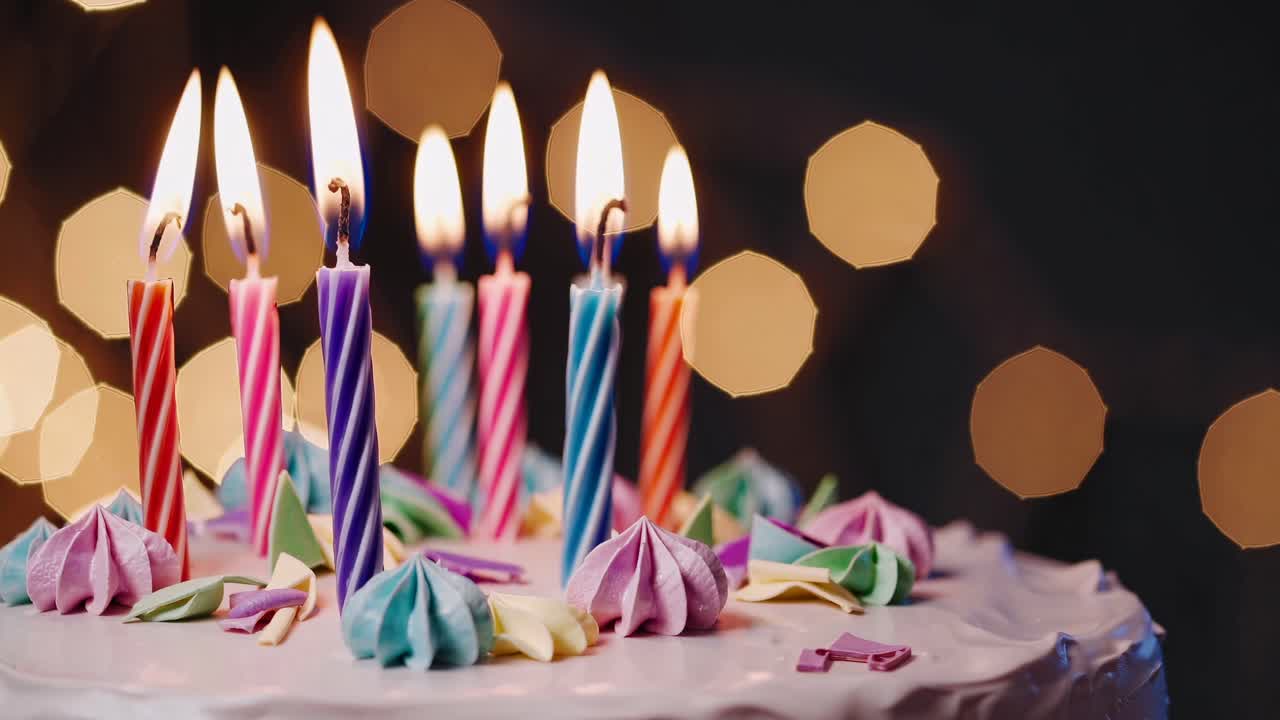 Video in primo piano di una torta di compleanno con candele accese e meringhe colorate, ripreso all'altezza degli occhi