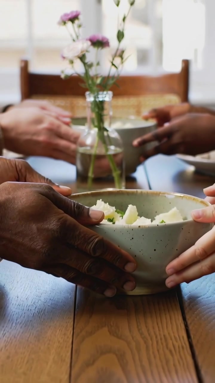 Vertical video: Reaching hands passing speckled bowl across home table with glass vase