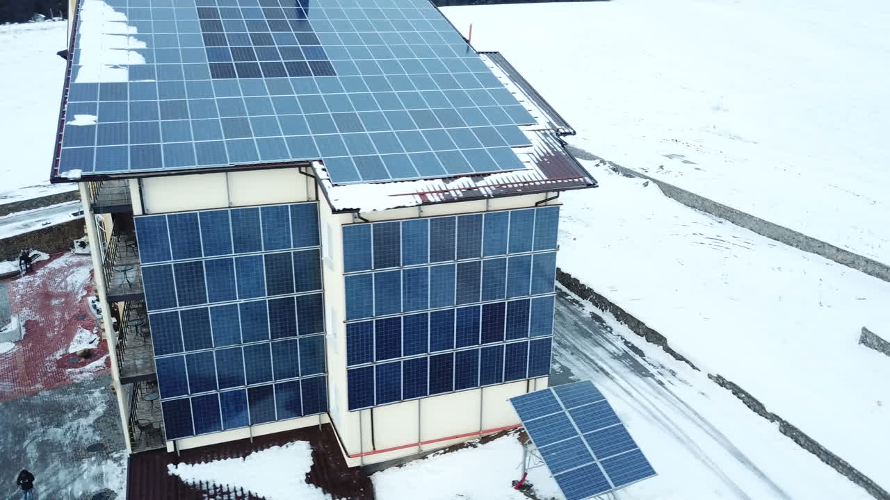 Hotel complex in the mountains with solar panels on the snow. Rows of snow covered solar panels in a small solar power plant.