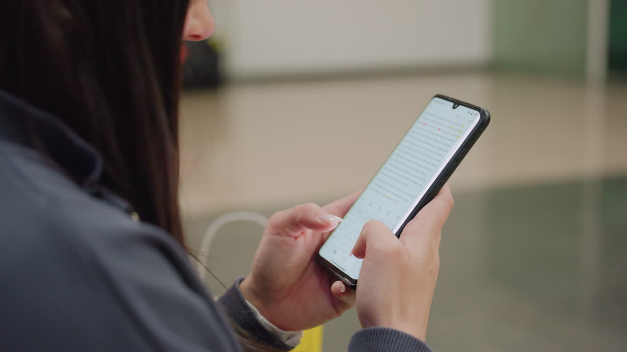 Close up of woman holding smartphone and typing with focused attention while seated indoors, composing message or email, displaying digital lifestyle and modern communication in quiet setting