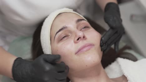 close-up scene of female cosmetologist who is making a face massage for a woman who lies with an opened eyes