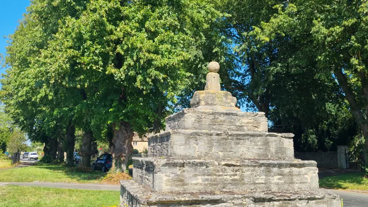 Panoramic view of Bainton, Cambridgeshire, showing village houses and the historic Butter Cross on a bright sunny summer day in rural England