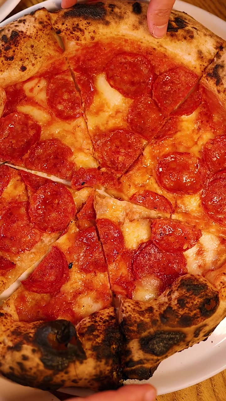 Ripresa dall'alto di persone che prendono fette di pizza napoletana al salame piccante da un piatto bianco.