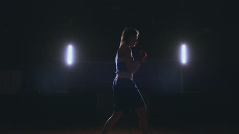 training a beautiful female boxer doing punches in a dark room. steadicam shot. preparation for self-defense and fight in the ring