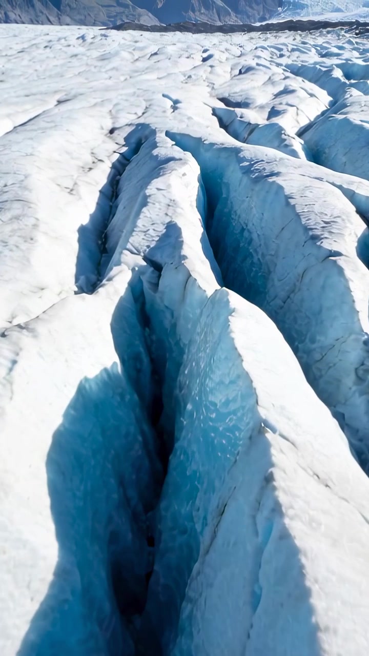 Vertical video: Gliding drone moving forward along ice ridge, revealing crevasse for closer detail