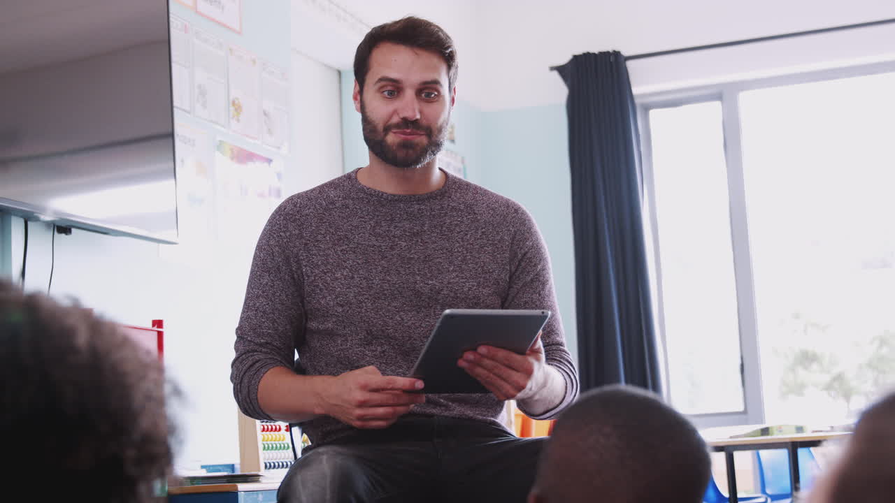 maestro masculino con una tableta digital enseña a un grupo de alumnos de primaria uniformados en el aula de la escuela