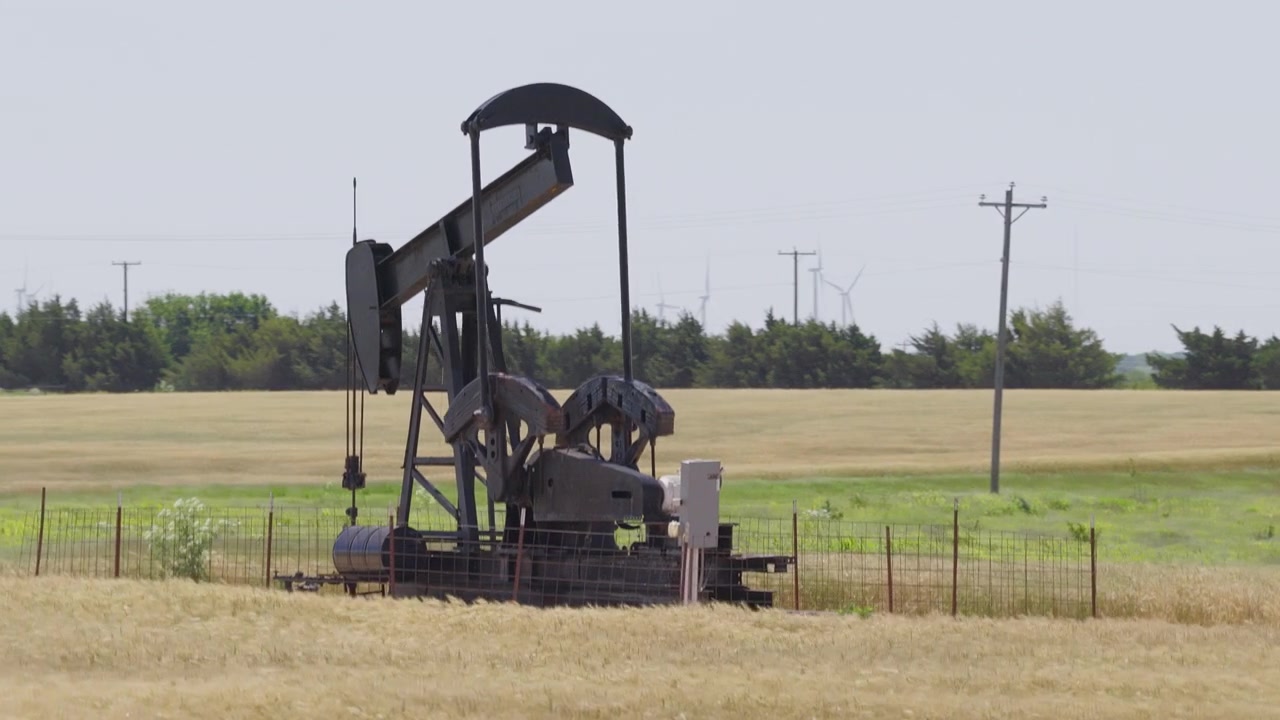 Drone 4K of a wheat field with two oil pump jacks and wind turbines in the background.