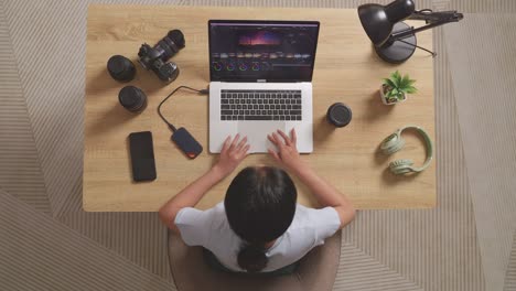 top view of asian woman color grading having a backache while sitting in the workspace using a laptop next to the camera editing the video at home