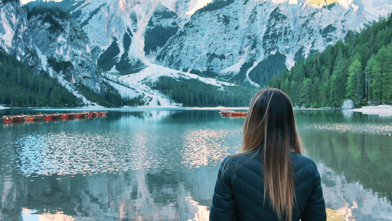 Solitary woman standing on the shore of Lake Braies, admiring the mountain reflection in the water