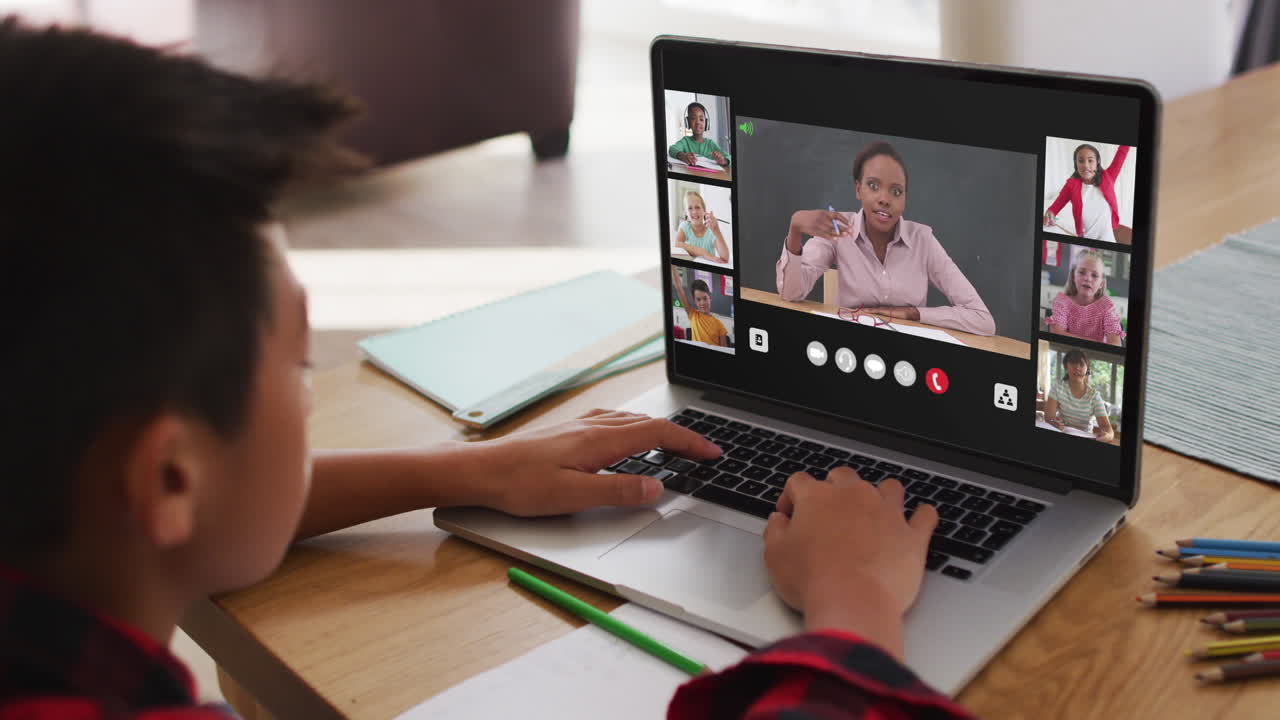 Schoolboy using laptop for online lesson at home, with diverse teacher and class on screen