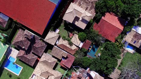 4k aerial footage of modern rooftops in búzios on a bright sunny day. the scene features pools, stylish houses, and a helipad in the corner, showcasing a luxurious lifestyle in vibrant detail.