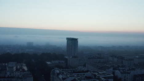 Forwards-fly-above-urban-neighbourhood,-tall-apartment-house-protruding-above-development.-Foggy-morning-background.-Warsaw,-Poland