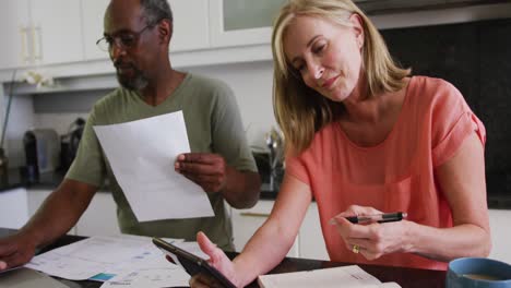 diverse senior couple using tablet computer paying bills in kitchen