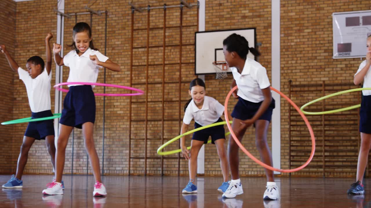 Schooljonge geitjes die met hoelahoep spelen binnen in basketbalhof