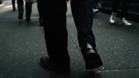 siguiendo un primer plano de las piernas de un hombre caminando por una concurrida acera de una gran ciudad.