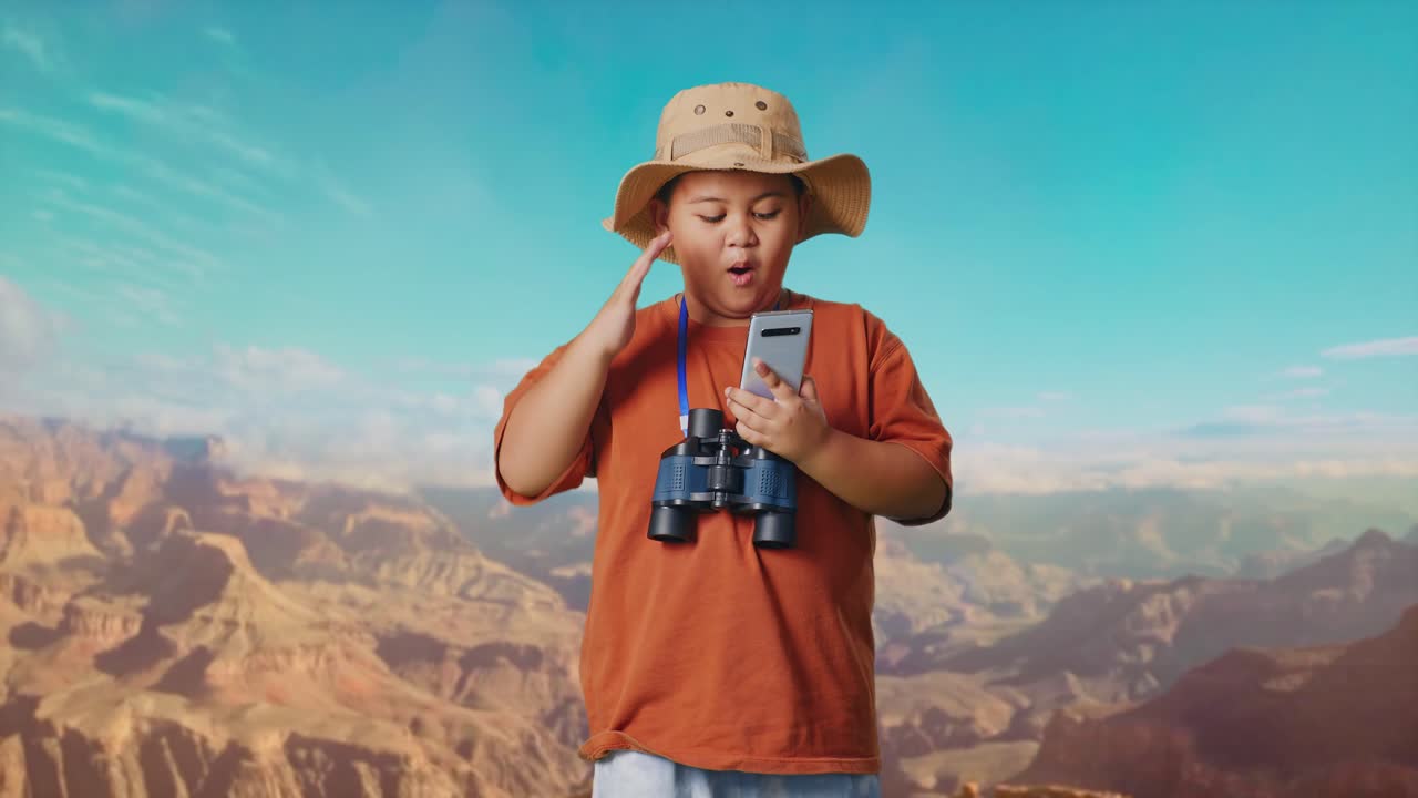 Asian Boy With A Hat And Binoculars Looking At Smartphone Then Saying Wow. Boy Researcher Examines Something While Traveling At The Top Of Mountain, Travel Tourism Adventure Concept
