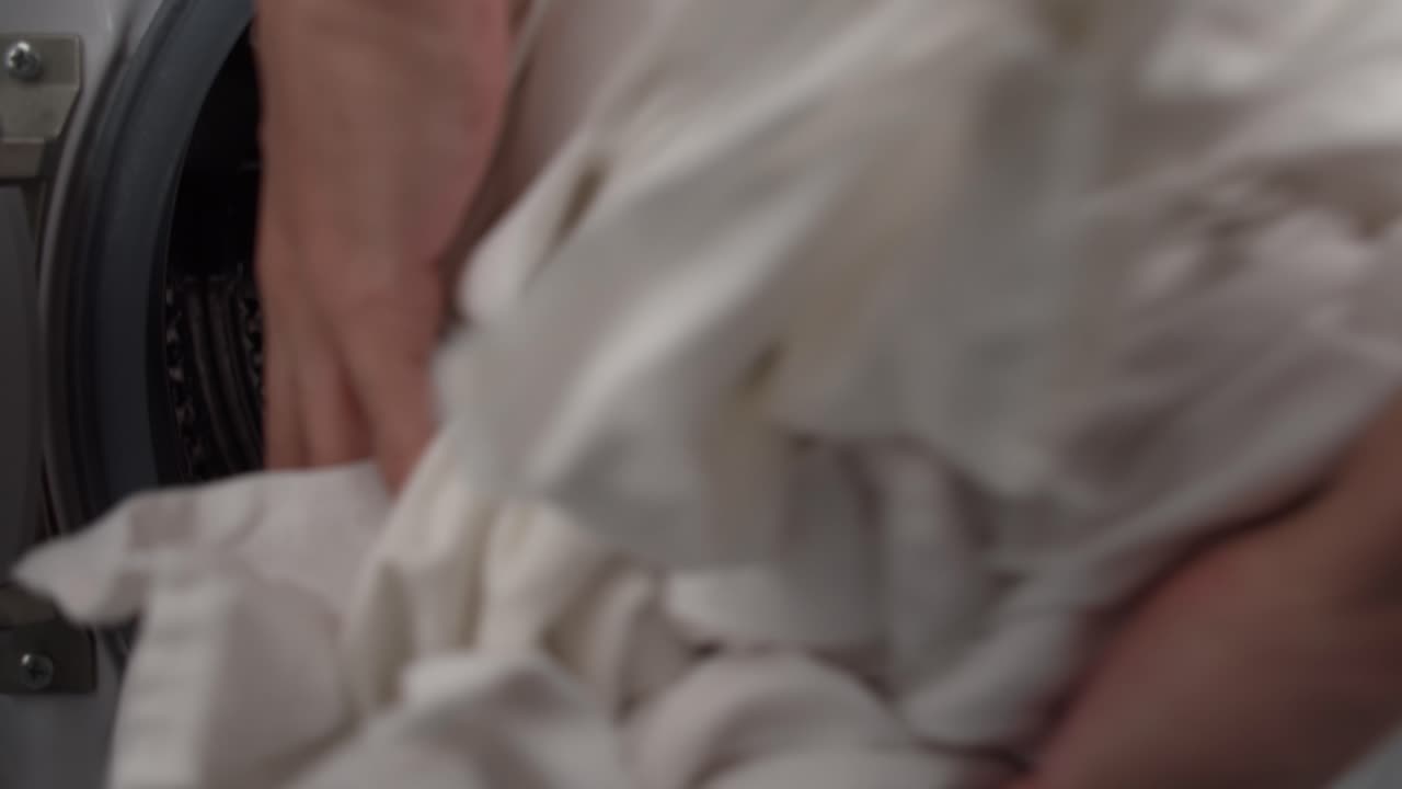 Hand putting sheet in washing machine. Close up, static