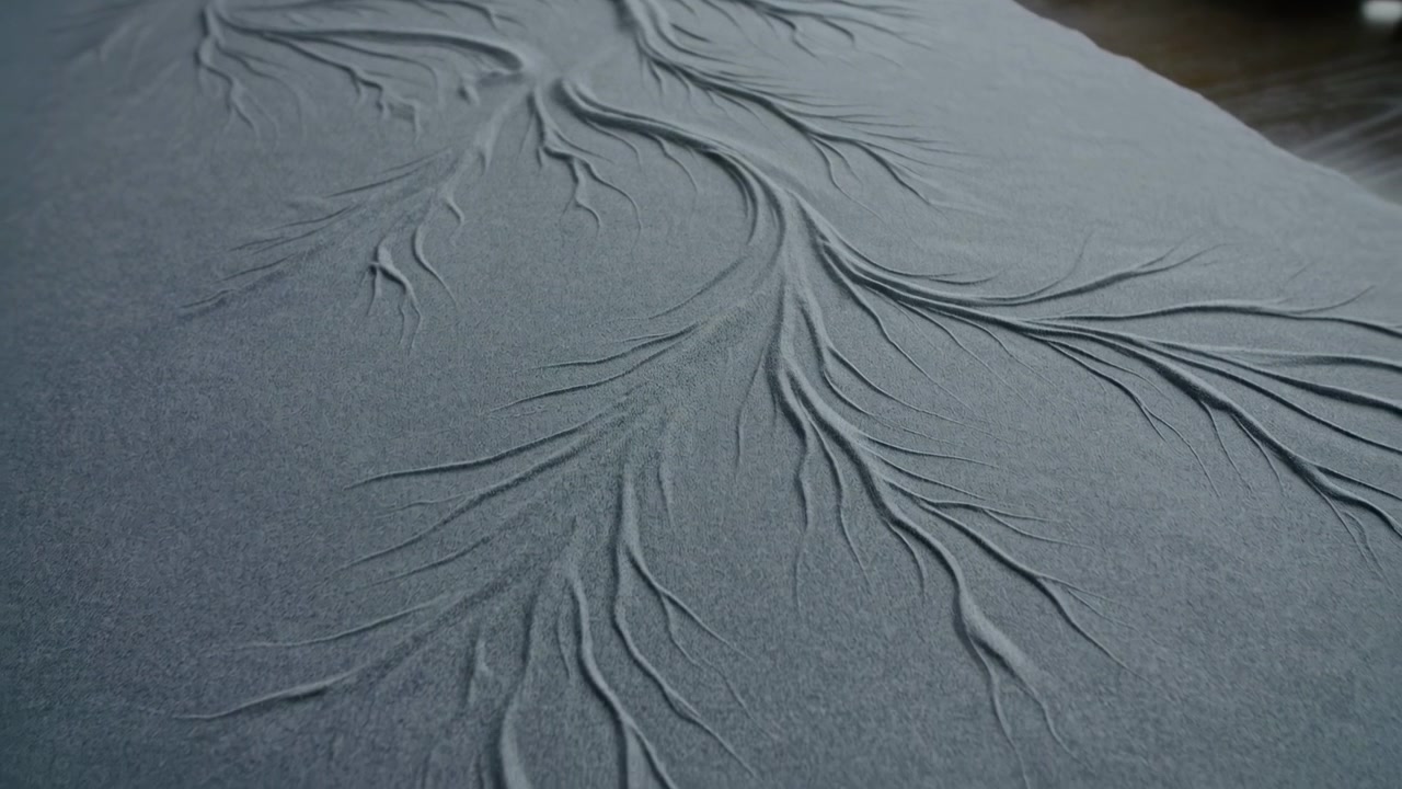 Soft indoor light reveals a large piece of gray fabric with visible folds and creases spread diagonally over a flat surface, creating a muted textured