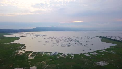 panning aerial view of floating fish net cages in indonesia lake and rice fields