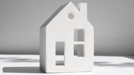 close-up of a ceramic figurine in the form of a house with windows and a doorway on a light gray background with a shadow from a plant.