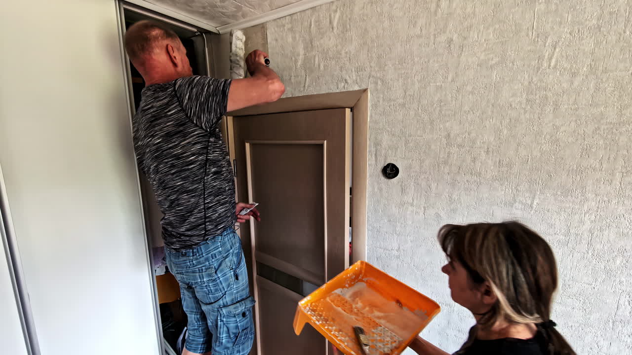 Wife and husband doing room renovation with wallpaper together applying glue on wall