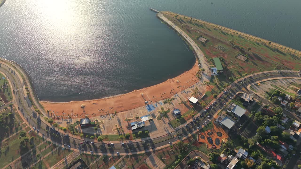 Bahía El Brete in Posadas, Argentina, with Avenida Costanera sand bay, walkways, sports courts and Paraná River seen in a top-down drone shot highlighting urban layout and shoreline use