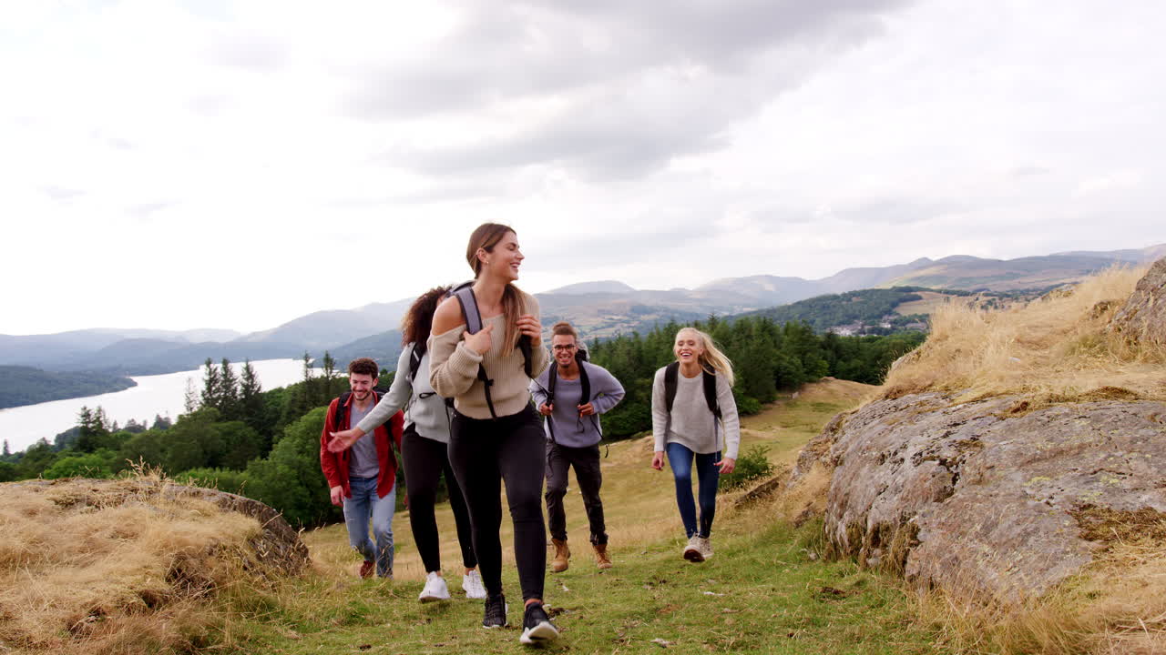 A multi ethnic group of five young adult friends smile while hiking across a field to the summit during a mountain hike, close up