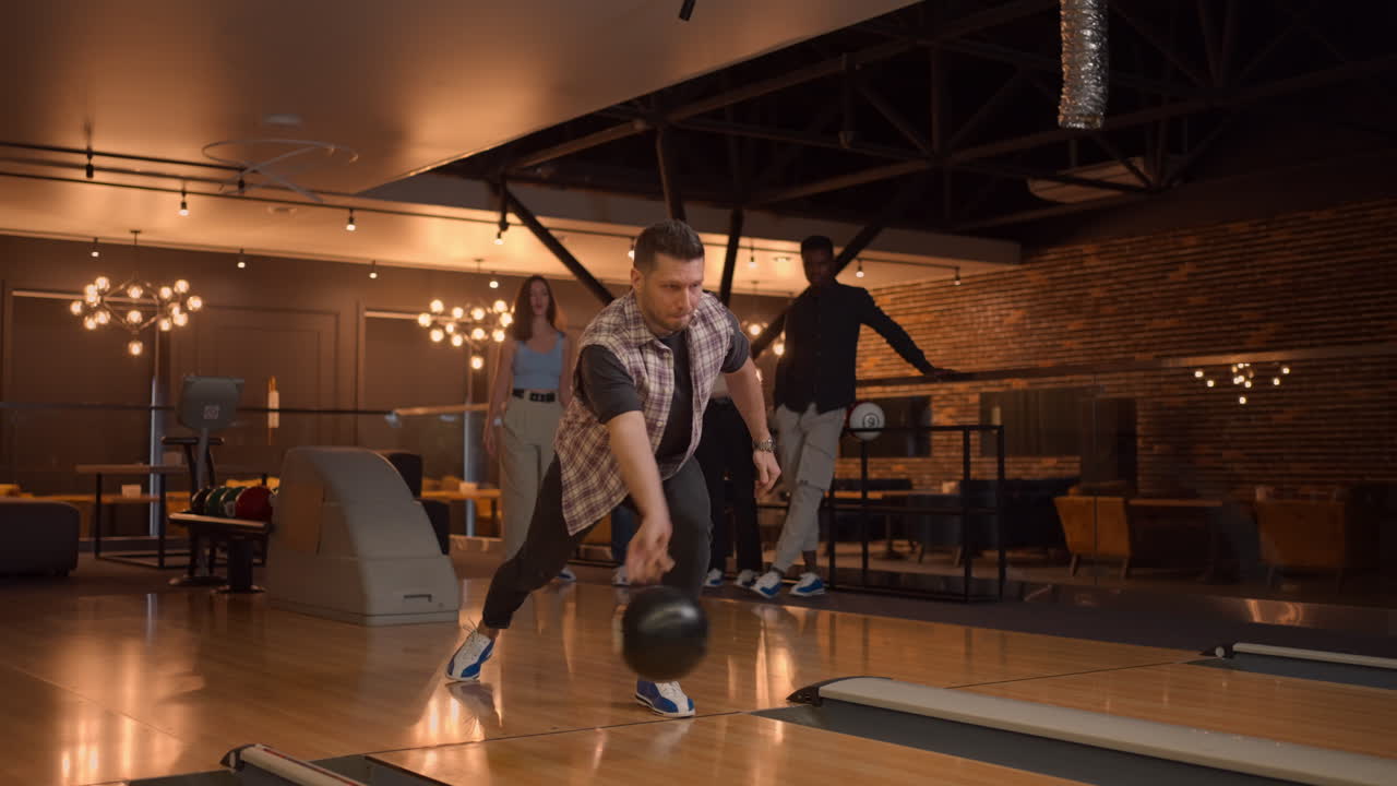 A Caucasian young man makes a throw in a bowling club and enjoys emotionally knocking out pins with a ball