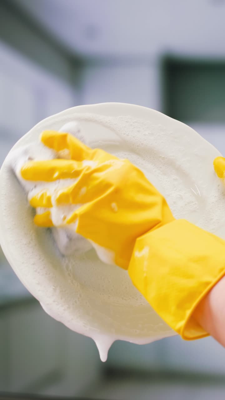 Hand in Yellow Glove Washing a White Plate with Soap Suds