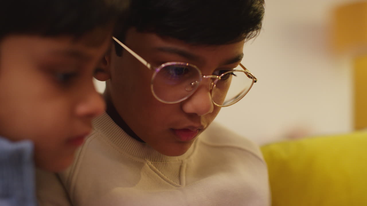 dos niños pequeños sentados en el sofá en casa jugando juegos o transmitiendo a una tableta digital 3