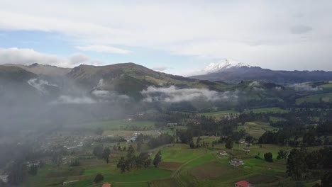 foggy and cloudy valley landscape with small houses in aerial drone view