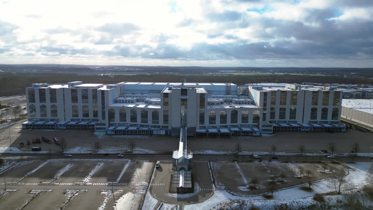 Large distribution center like an industrial castle with loading docks and parking lot under a cloudy sky in winter. Fantastic aerial view flight drone shot footage from above