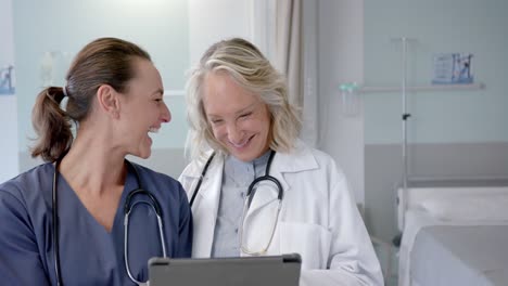 Happy-caucasian-female-doctors-in-discussion-using-tablet-in-hospital-room,-slow-motion