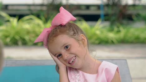 small-girl-puts-head-on-hand-and-laughs-near-swimming-pool