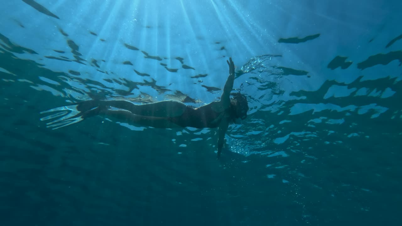 한 여성이 수영장에서 물속을 헤엄치고 빛이 물을 통해 필터링하여 조용한 장면을 만니다.