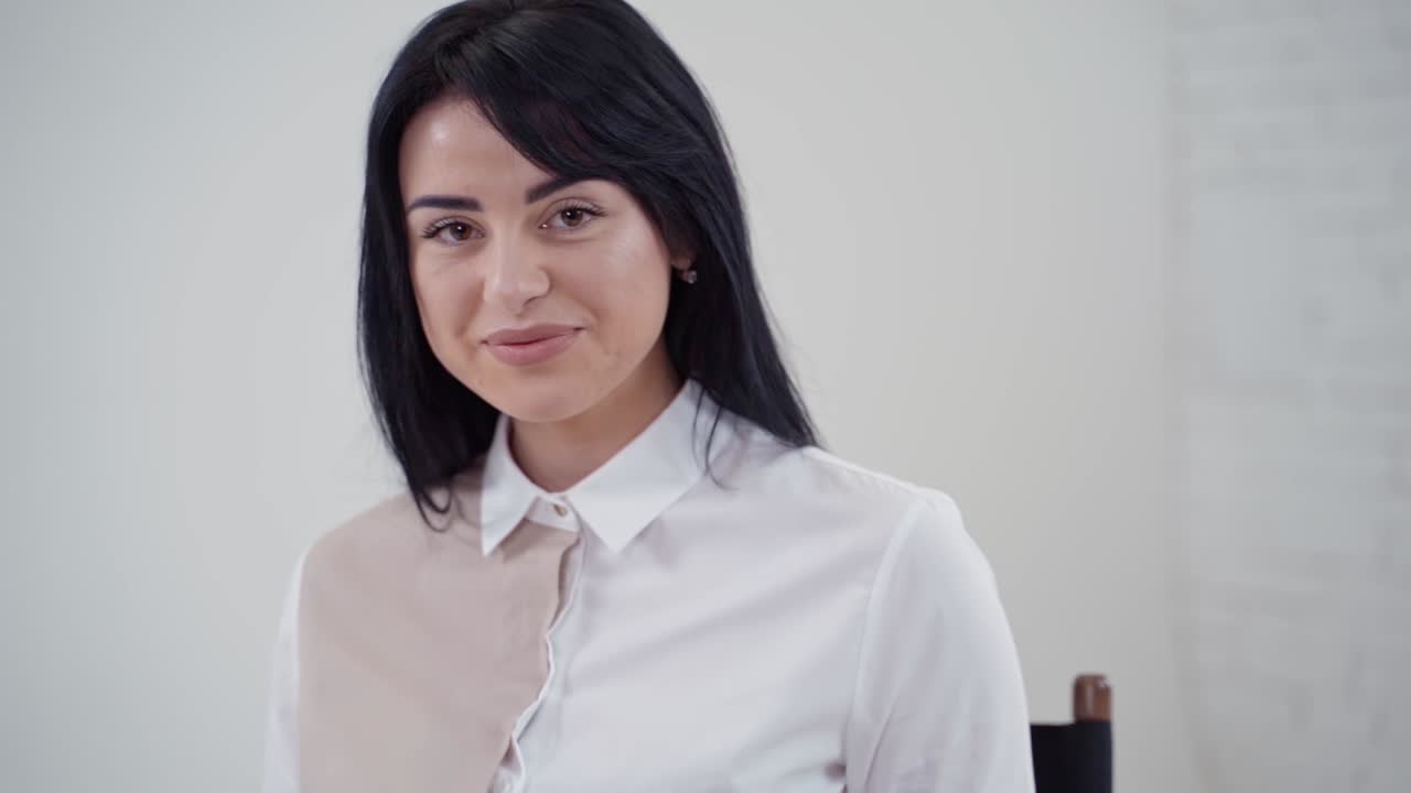 Portrait of a beautiful dark-haired girl in studio. Young woman in white blouse and short skirt sitting on the chair with laptop on light background.