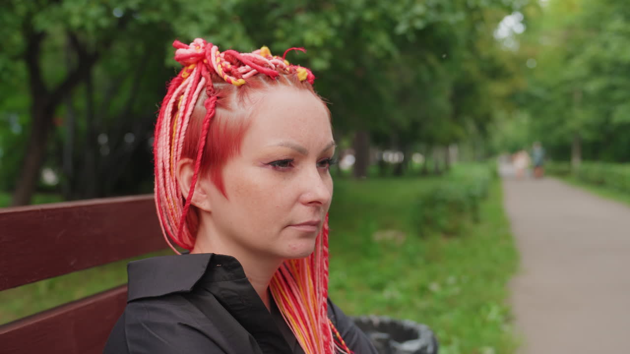 다채로운 땋은 머리를 한 쾌활한 표정의 백인 여성, 나무 근처에서 생기 넘치는 땋은 머리를 한 백인 여성, 야외에서 즐거운 순간을 만끽하는 밝게 땋은 머리와 풍부한 제스처를 가진 여성