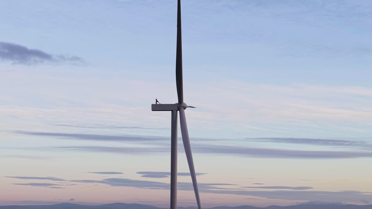 Solitary figure atop wind turbine at sunset, symbolizing solitude and renewable energy
