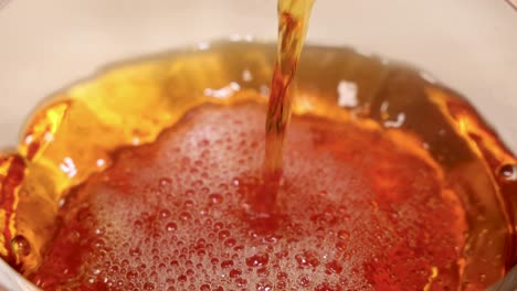 golden liquid streams into a glass, creating bubbles and a rich amber hue under soft lighting