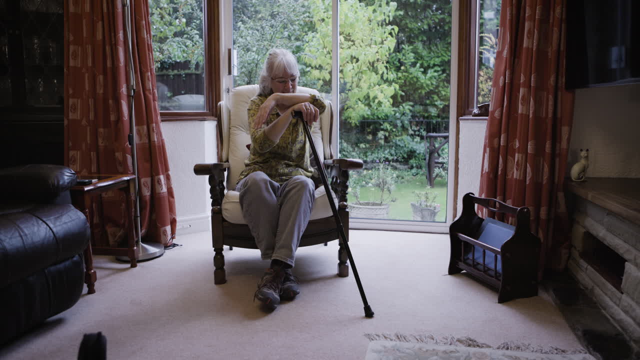 Sad senior woman sitting in armchair with walking stick