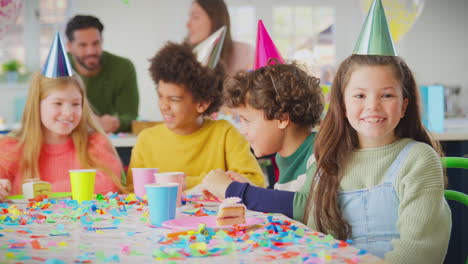 girl blowing confetti at camera at birthday party with friends and parents at home