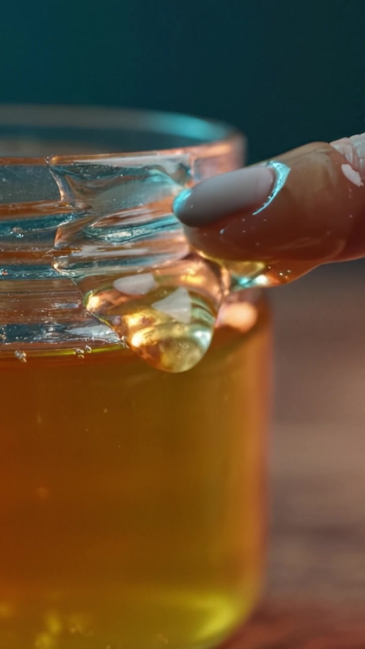 Miele dorato che cola da un barattolo di vetro: un viaggio ravvicinato nel dolce nettare della natura, che mostra il suo colore ricco e la consistenza viscosa, perfetto per la cucina e la salute