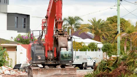 a red excavator removes palm plants and debris at a residential construction site in gold coast, australia, during daylight with steady camera framing