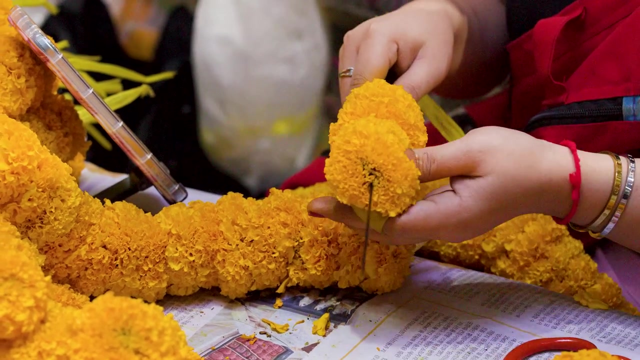 Primo piano di mani che infilano fiori di calendula gialli su una ghirlanda al Mercato dei Fiori di Bangkok