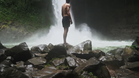 El-Hombre-Se-Para-Frente-A-La-Poderosa-Cascada-De-La-Selva-Tropical-Con-La-Niebla-Soplando