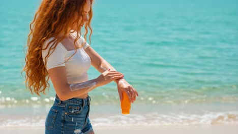 A Young Woman Applying Sunscreen on Her Arm While at the Beach, Embracing Sun Safety with Radiant Curls and a Bright Ocean Background