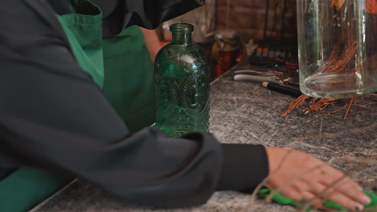 Arranging stems and tidying floral tools. Carefully wiping and organizing floral supplies on counter. Meticulously cleaning and arranging floral containers and tools to ensure neat setup