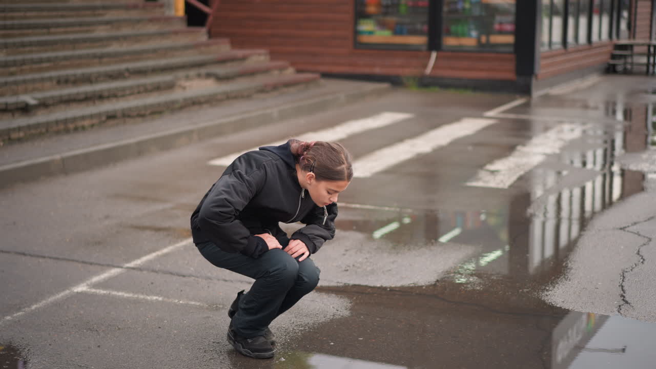 Jovem mulher examina o reflexo na poça. Jovem para para examinar a superfície reflexiva sob seus pés. Garota para para observar a poça espelhada precisamente onde está.